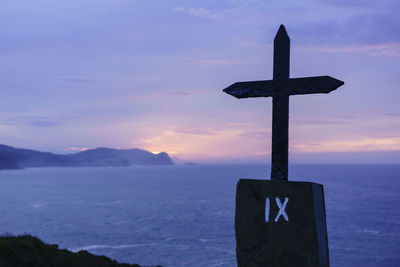 Cross on sea against sky during sunset