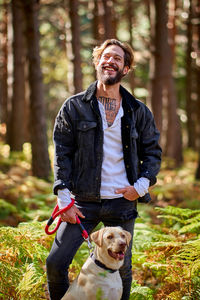 Portrait of young tattoed man with his dog in the forest