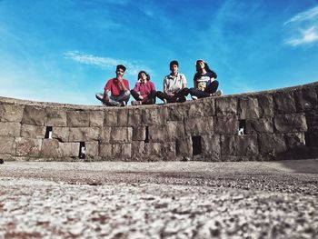 People sitting on retaining wall against sky