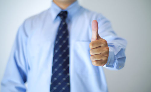 Close-up of midsection of businessman showing thumbs up against white background