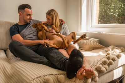 Smiling young couple with vizsla dog relaxing on bed at home