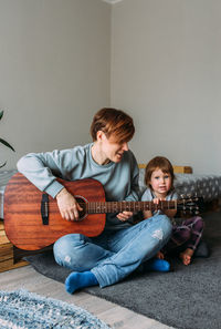 Little girl plays the guitar with her mother on the floor at home