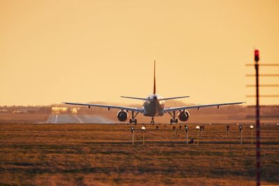 Airplane flying at airport against sky during sunset