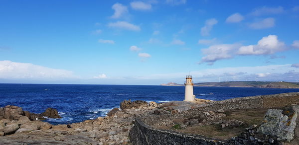 Lighthouse on cliff by sea against blue sky