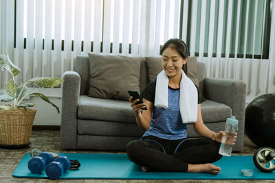 Full length of smiling young woman sitting on sofa at home