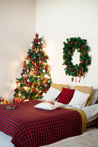 Christmas bedroom interior in white and red colors. double bed with plaid blanket and christmas tree
