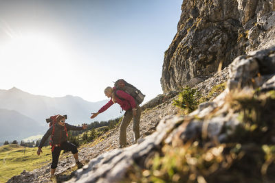 People on rock by mountains against sky