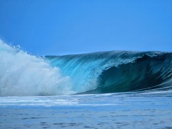 Breaking wave at sea against clear blue sky