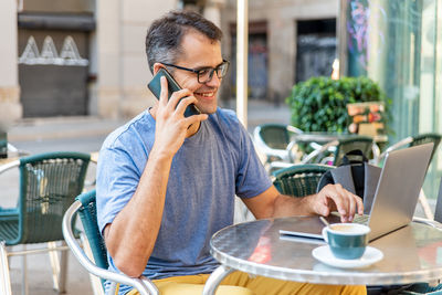 Smiling man talking on phone while sitting at cafe