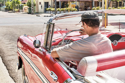 Man sitting in red vintage 1957 car on street of resort town varadero, cuba.