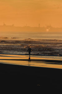 Silhouette woman walking at beach against sky during sunset