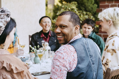 Portrait of smiling gay man looking over shoulder by friends during dinner party in back yard