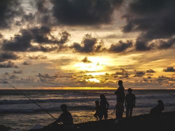 Silhouette people on beach against sky during sunset