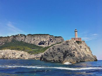 Lighthouse by sea against clear blue sky