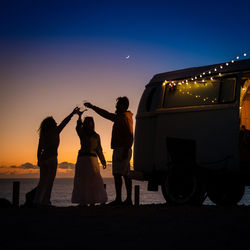 Silhouette mature friends toasting outside motor home at night
