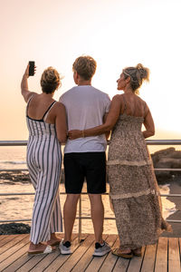 Beautiful mother with her twenty year old sons take a selfie by the sea at sunset - summer concept