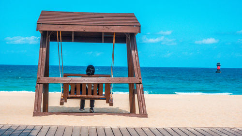 Rear view of woman sitting on swing at beach