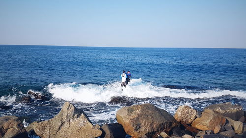 Rear view of men fishing in sea against sky