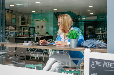 Woman using mobile phone while sitting on table at store