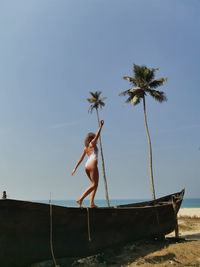 A girl walks along the edge of a boat on the beach in goa.