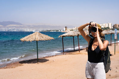 Rear view of woman photographing at beach against clear sky