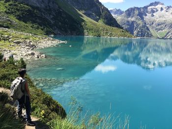 Rear view of mature woman with backpack standing at lakeshore against mountains