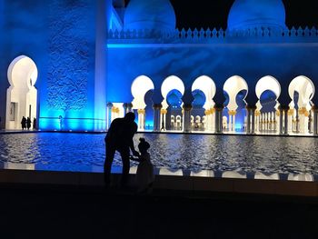 People walking by illuminated building at night