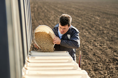 Male farmer pouring soybean seeds in machine at field