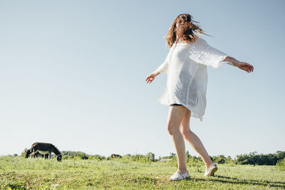 Woman with arms raised on field against clear sky