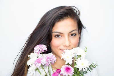 Close-up portrait of smiling young woman with flowers against white background