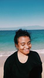 Portrait of smiling young woman on beach against sky