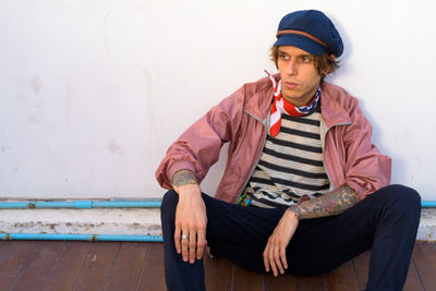 Portrait of young man sitting against wall