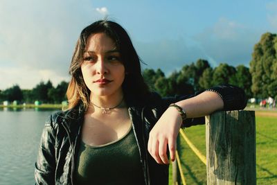 Thoughtful young woman looking away while standing by wooden post at park