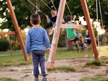 Rear view of boy standing by swing at playground