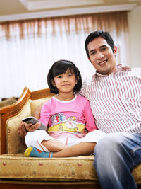 Father and daughter watching tv sitting on sofa at home