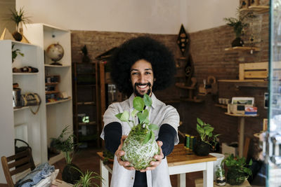 Cheerful man holding kokedama houseplant at home