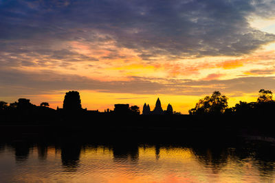 Silhouette trees by lake against orange sky