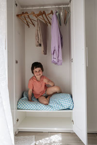 Small boy sitting in a wardrobe and looking out of the door