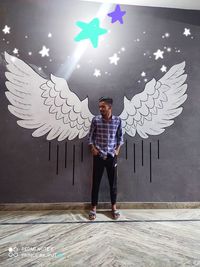 Full length portrait of young man standing against wall