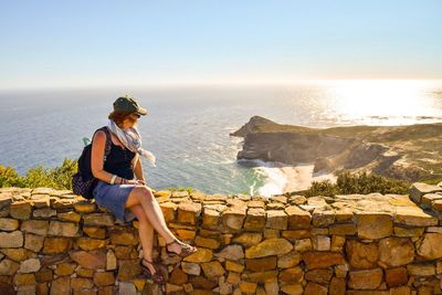 Woman standing on retaining wall by sea against sky