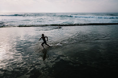 Silhouette boy at beach against sky