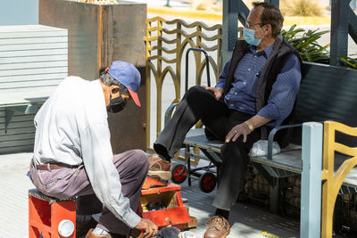 People sitting on seat getting shoe shine during covid pandemic.