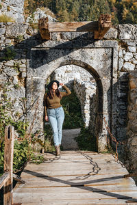Young woman standing on footbridge of old castle ruin, autumn, fall, earth tones, style.