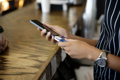 Midsection of woman using smart phone credit card reader in cafe