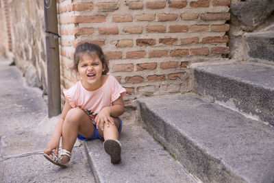 Portrait of girl sitting on brick wall