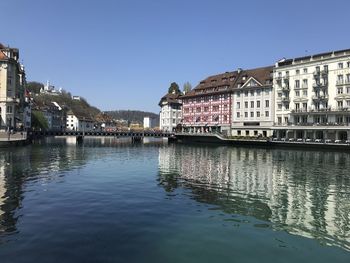 Reflection of buildings in river against clear blue sky