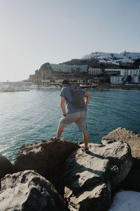 Woman standing on rock by sea against clear sky