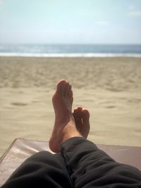 Low section of man relaxing on lounge chair at beach