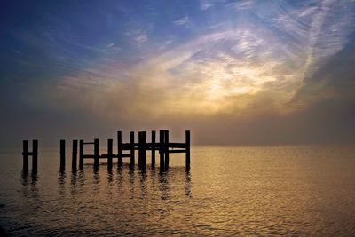 Silhouette wooden posts on sea against sky during sunset