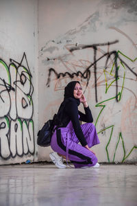 Woman looking away while sitting on floor against wall